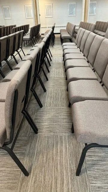 Rows of gray padded chairs in a carpeted waiting room or conference area, viewed down the aisle
