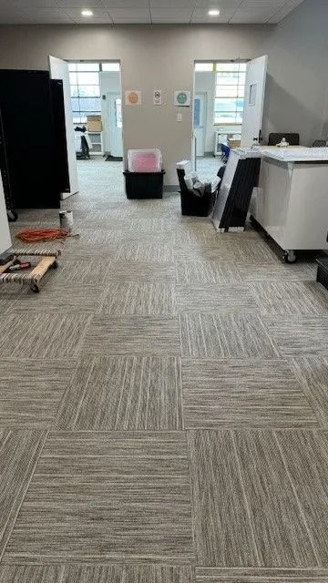 Empty office hallway with gray carpet, chairs, and open doorways leading to bright rooms.