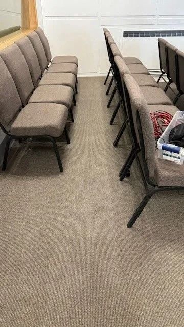 Two rows of beige cushioned chairs in a waiting room with carpeted floor and white walls