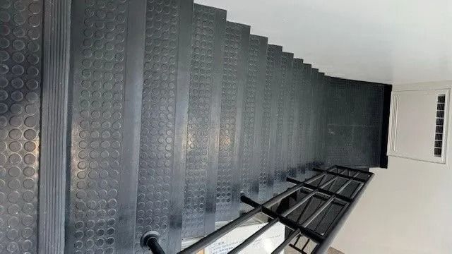 Row of dark gray lockers or cabinets along a bright white hallway wall, viewed at an angle.