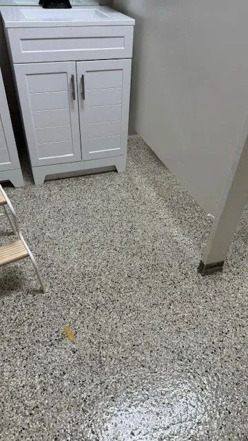 White bathroom vanity beside a speckled terrazzo floor and beige wall in a small room
