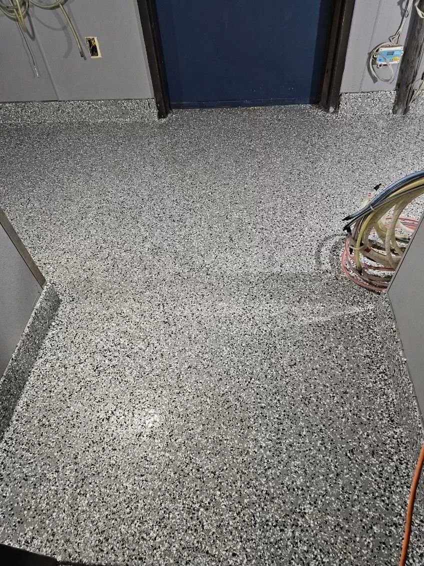 Grey speckled floor with a raised threshold leading to a blue door and wall-mounted cables on the right.