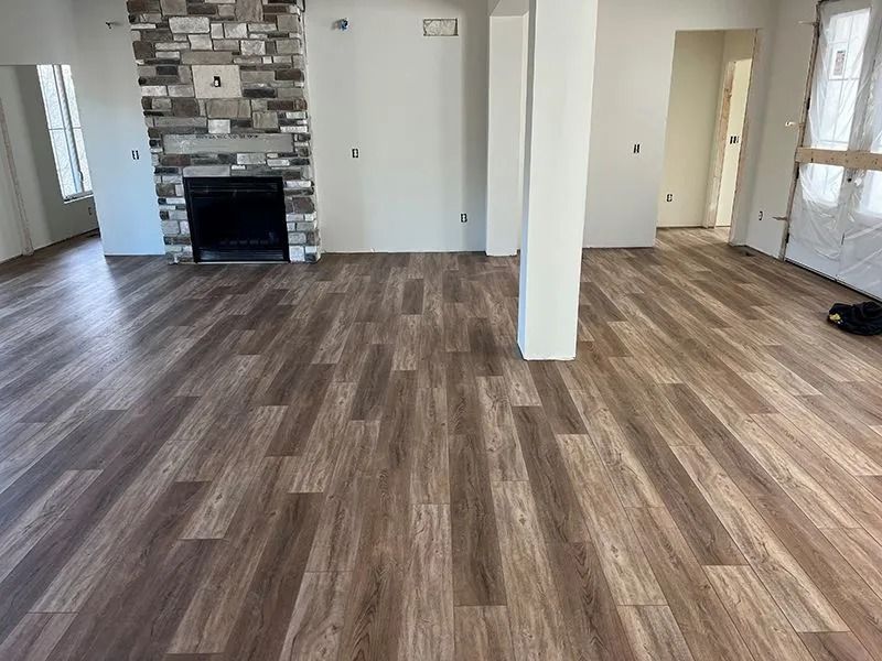 Empty living room with wood flooring, stone fireplace, white walls, and large windows.