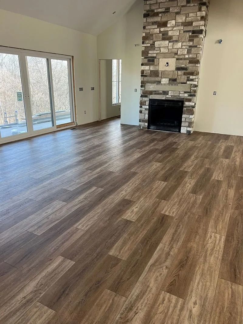 Empty living room with wood-look flooring, stone fireplace, and sliding glass doors.