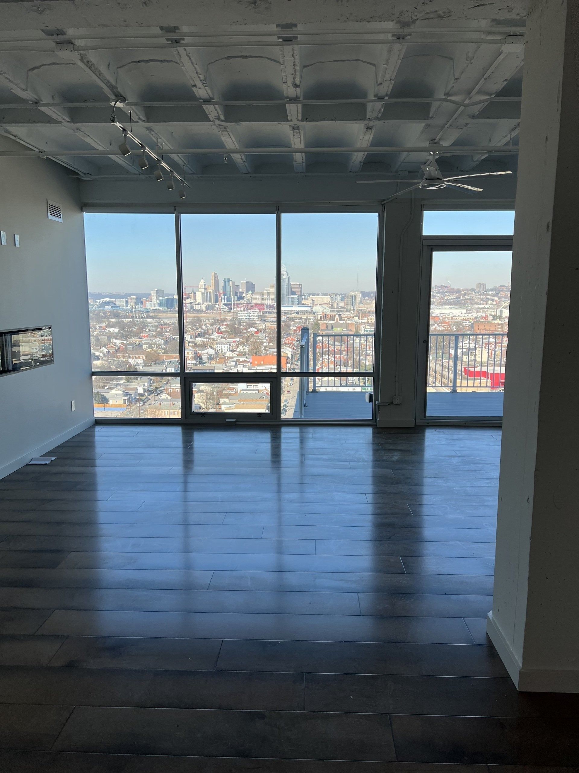 Empty room with large windows overlooking a city skyline and bright daylight.