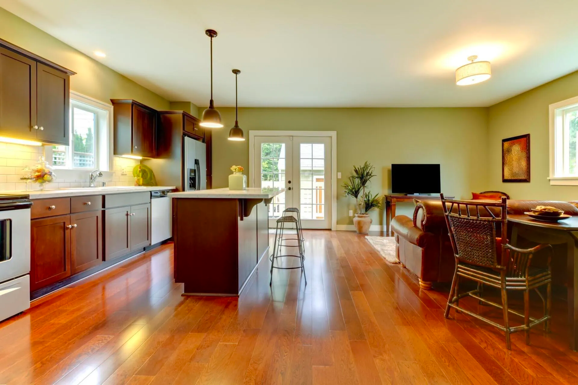 Open-plan kitchen and living room with hardwood floors, island seating, and a TV by French doors