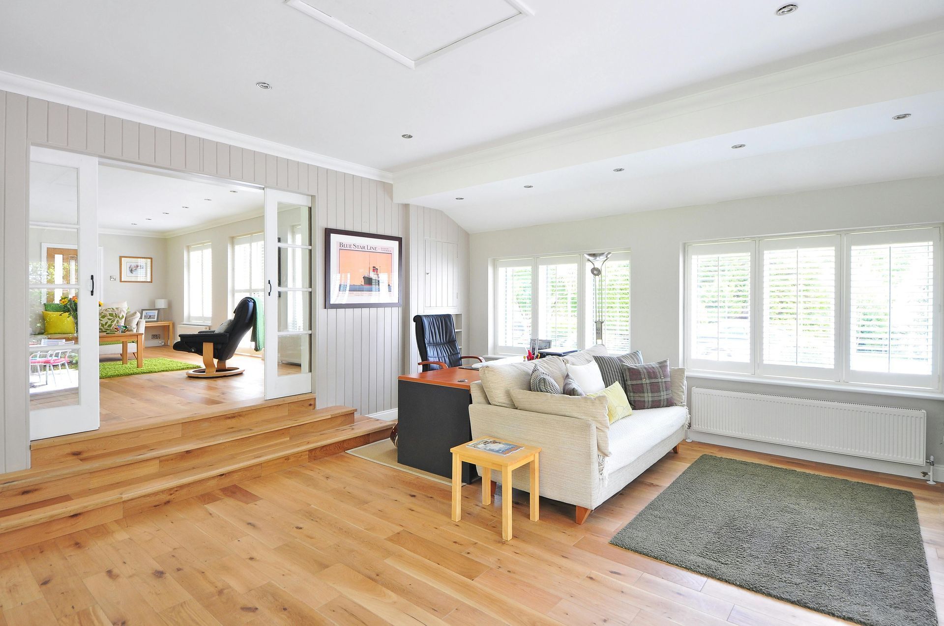 Bright open living room with white sofas, wood floors, large windows, and a raised seating area.