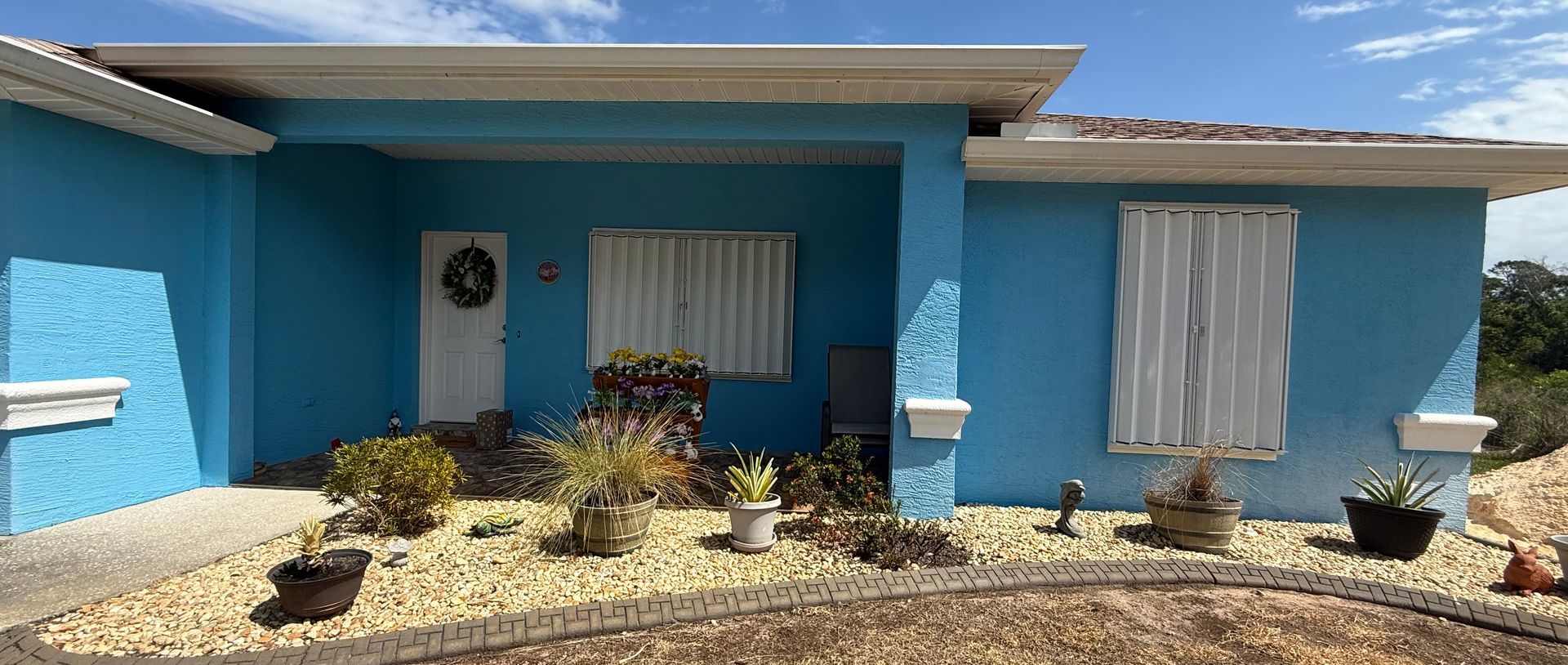 Bright blue house exterior with white trim, front porch, windows, and small landscaped yard.