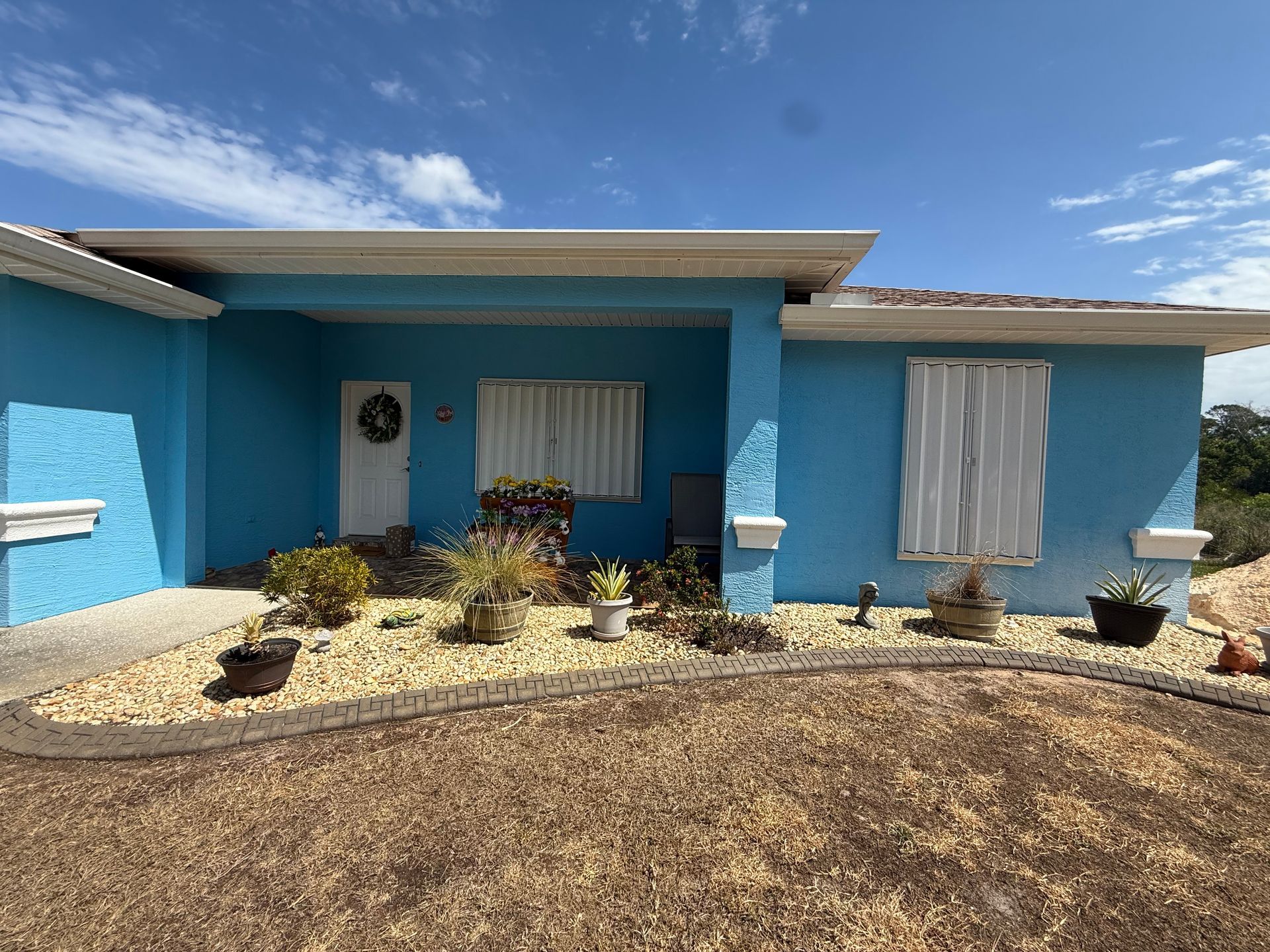 Blue single-story house with white trim, front windows, and desert landscaping under a bright sky