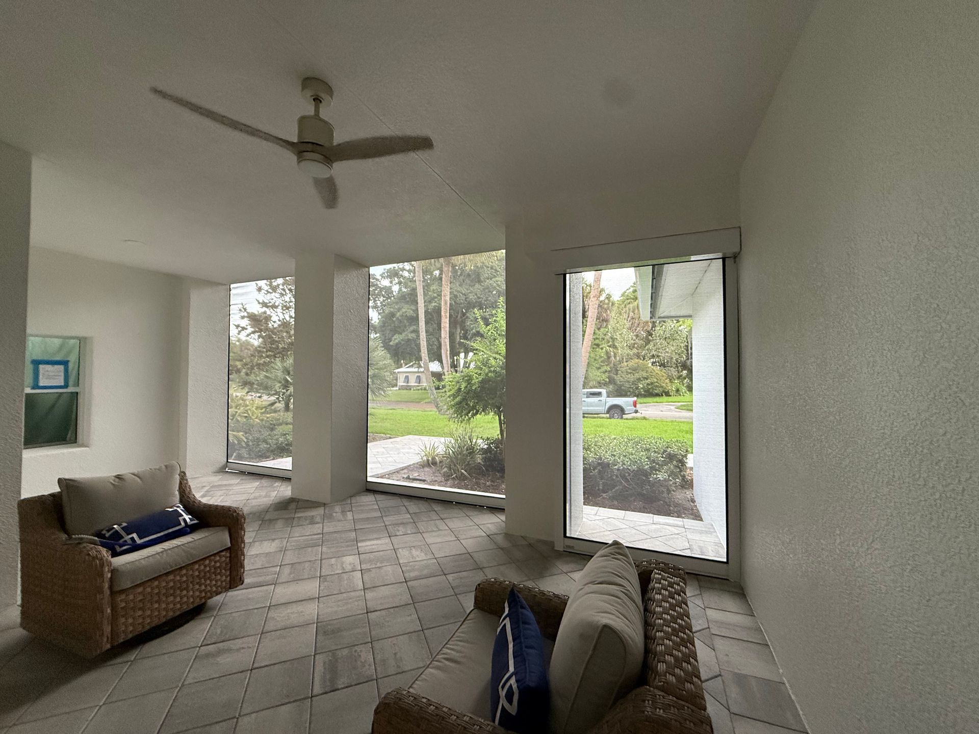 Covered patio with wicker seating, ceiling fan, and large windows overlooking a tree-lined yard.