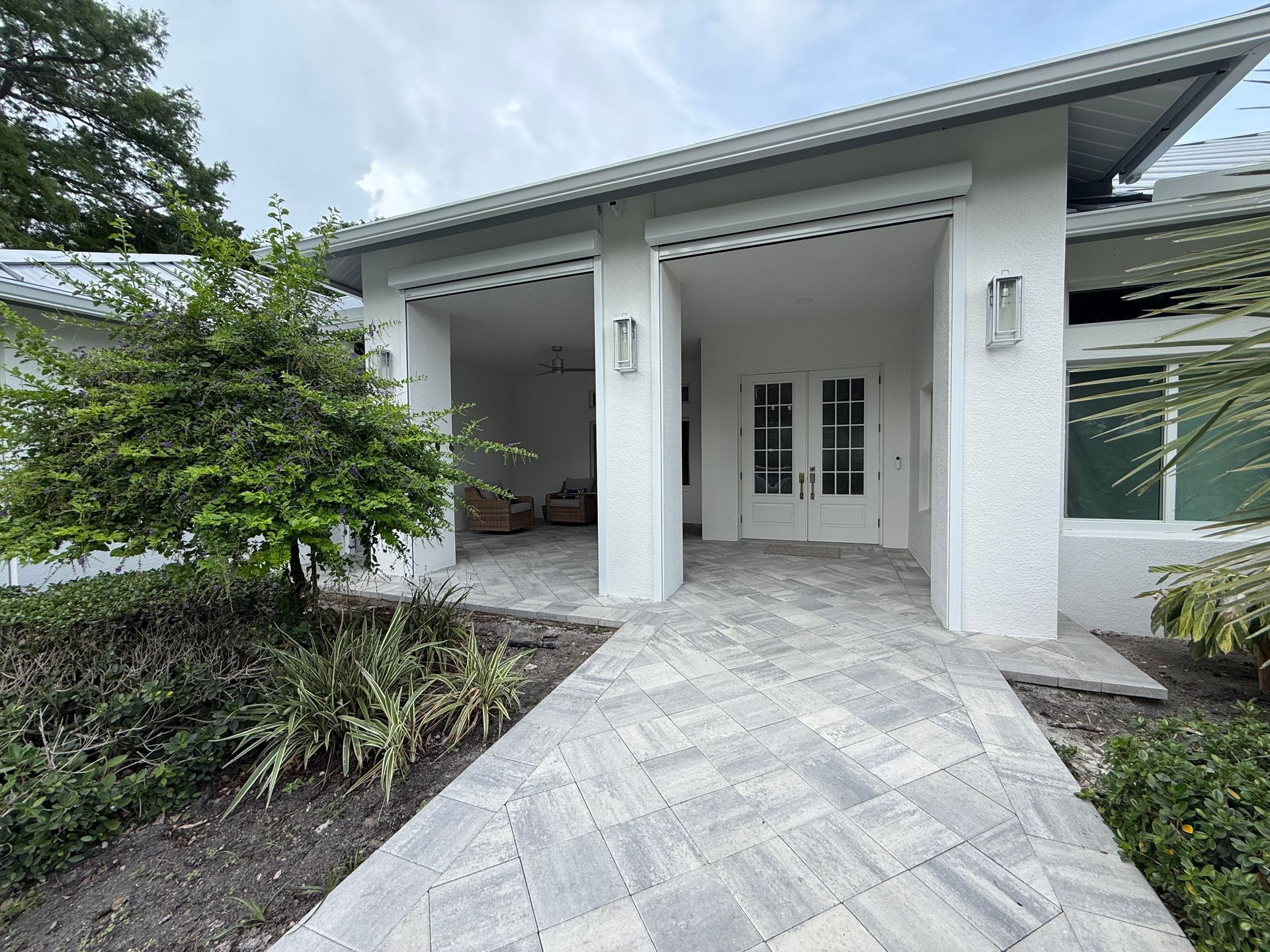 Covered front porch with white columns, paver walkway, and double glass doors on a modern house