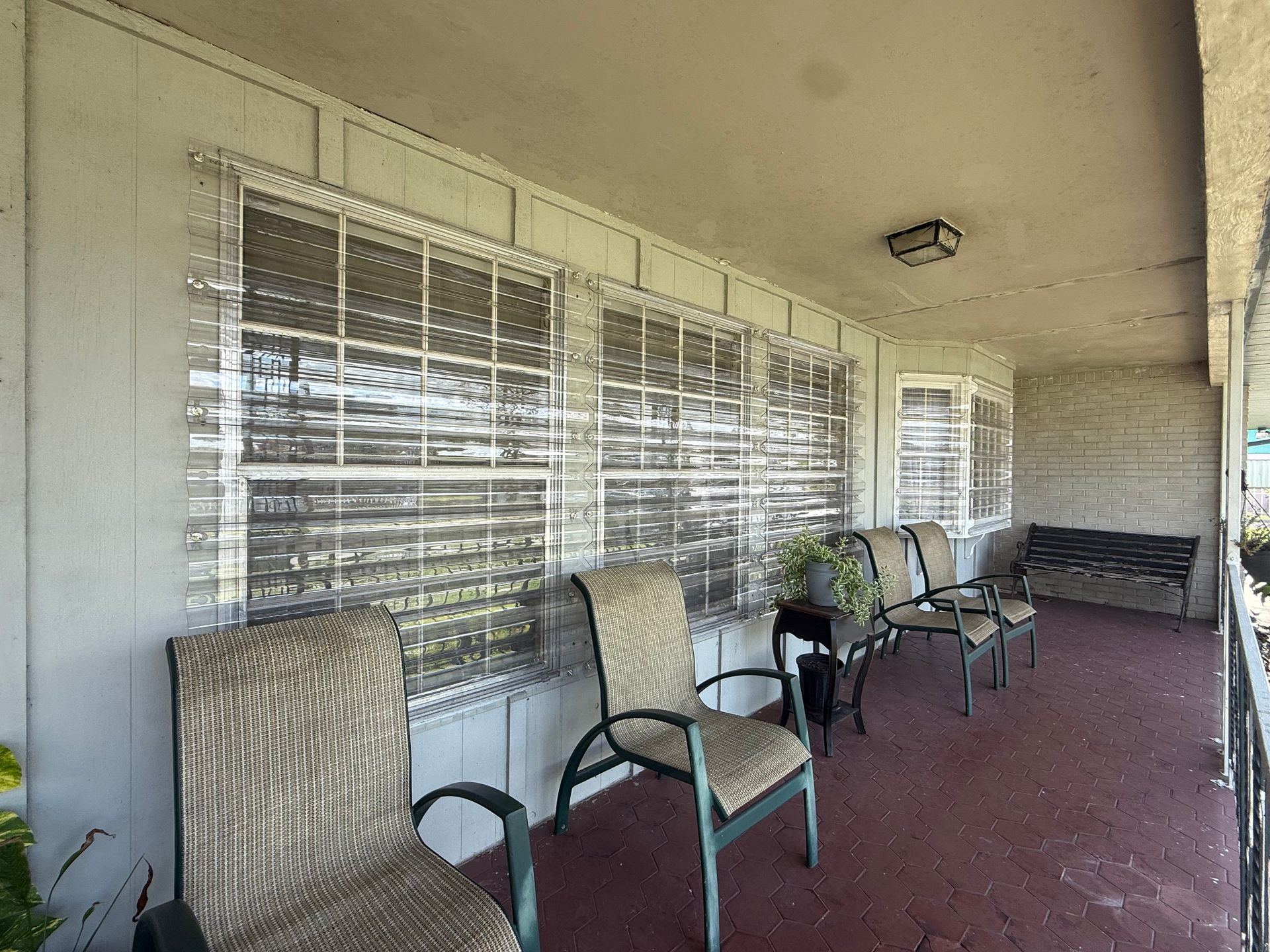 Porch with red floor, white walls, windows with blinds, and several chairs along the wall.