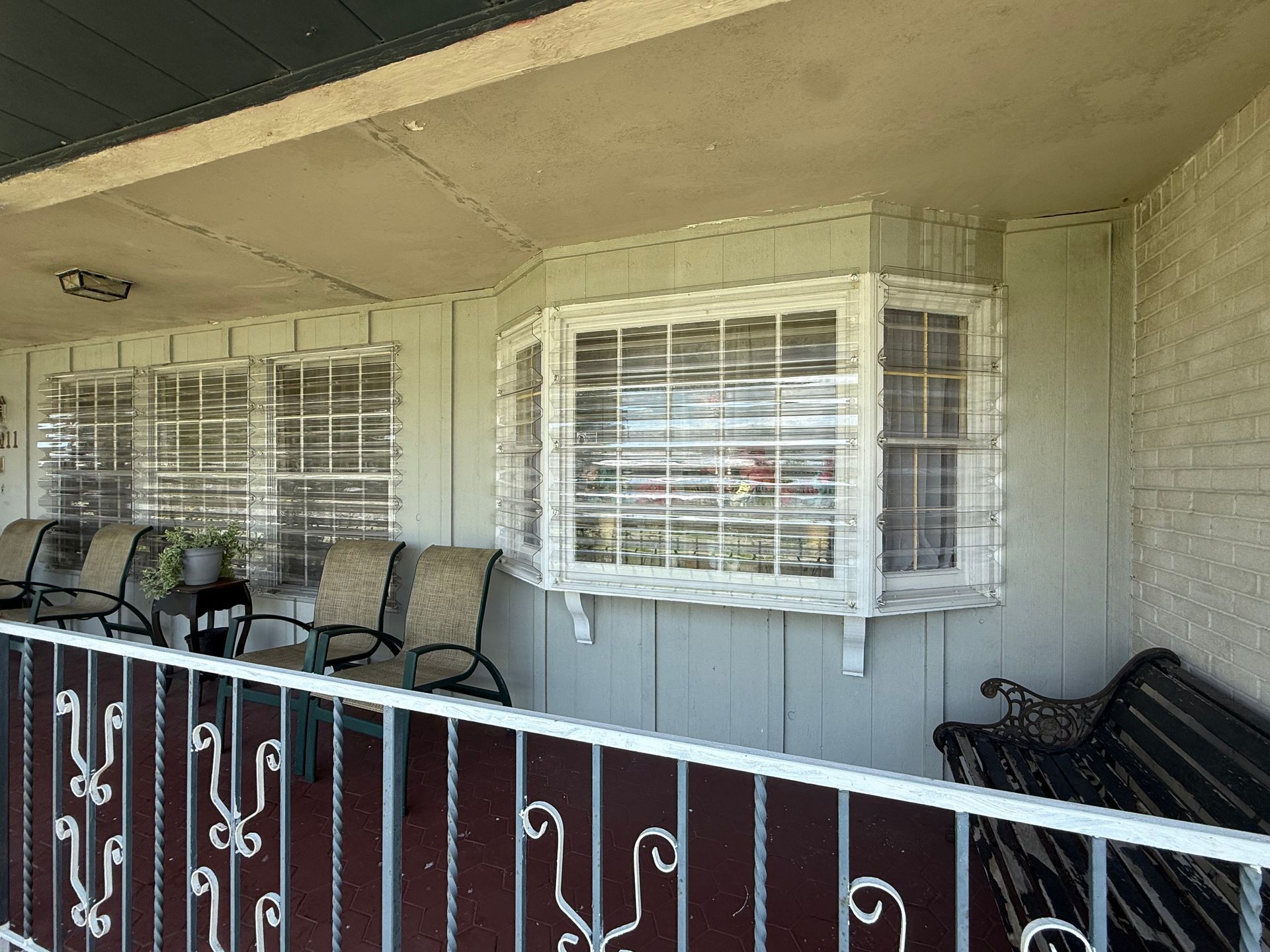 Covered porch with white siding, barred windows, and black metal chairs behind a red railing.