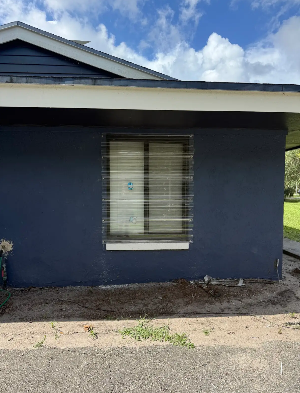 Blue house exterior with a white-trimmed window and cloudy sky above