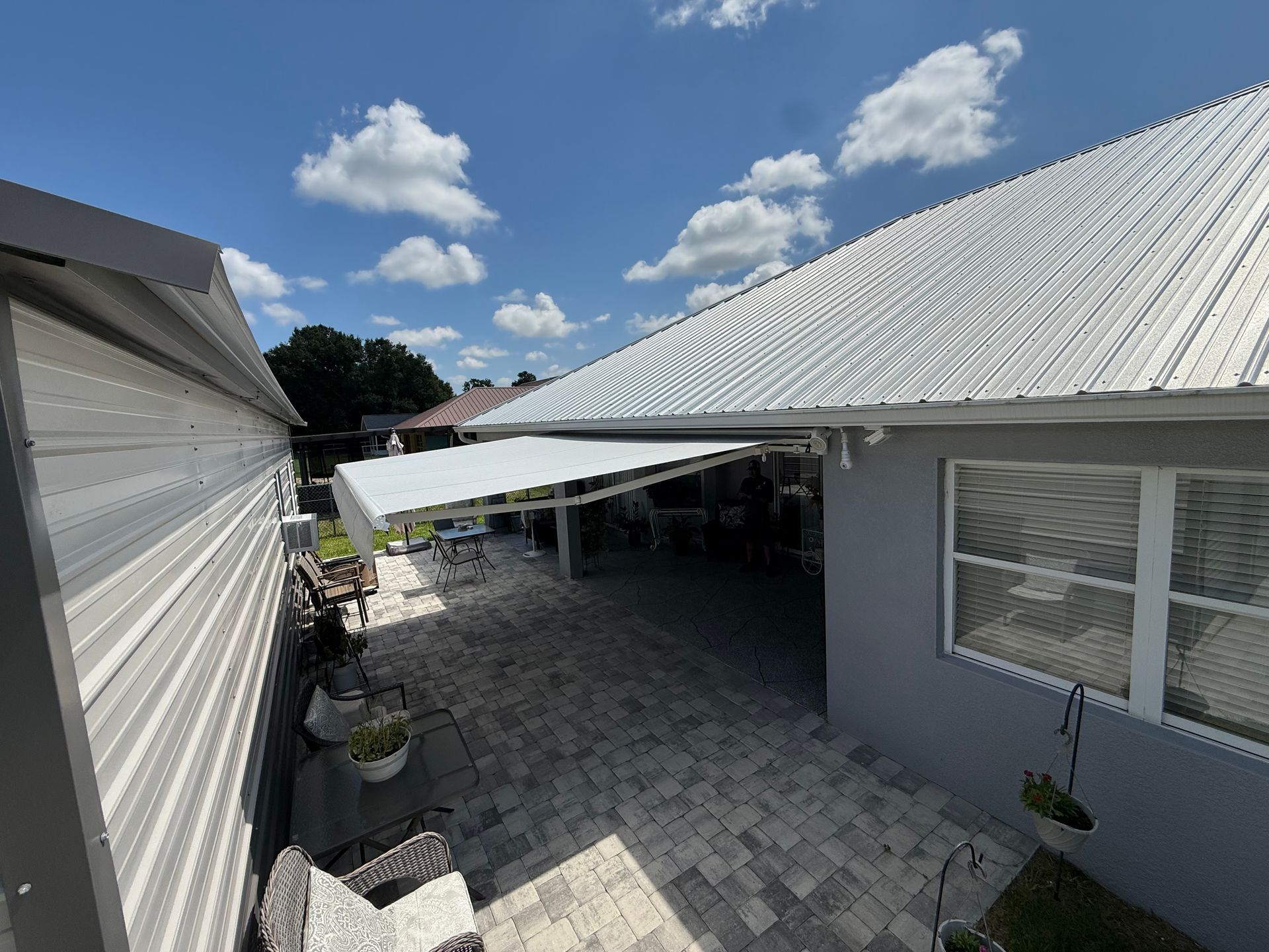 Courtyard between white buildings with a gray paver patio, awning, potted plants, and blue sky with clouds