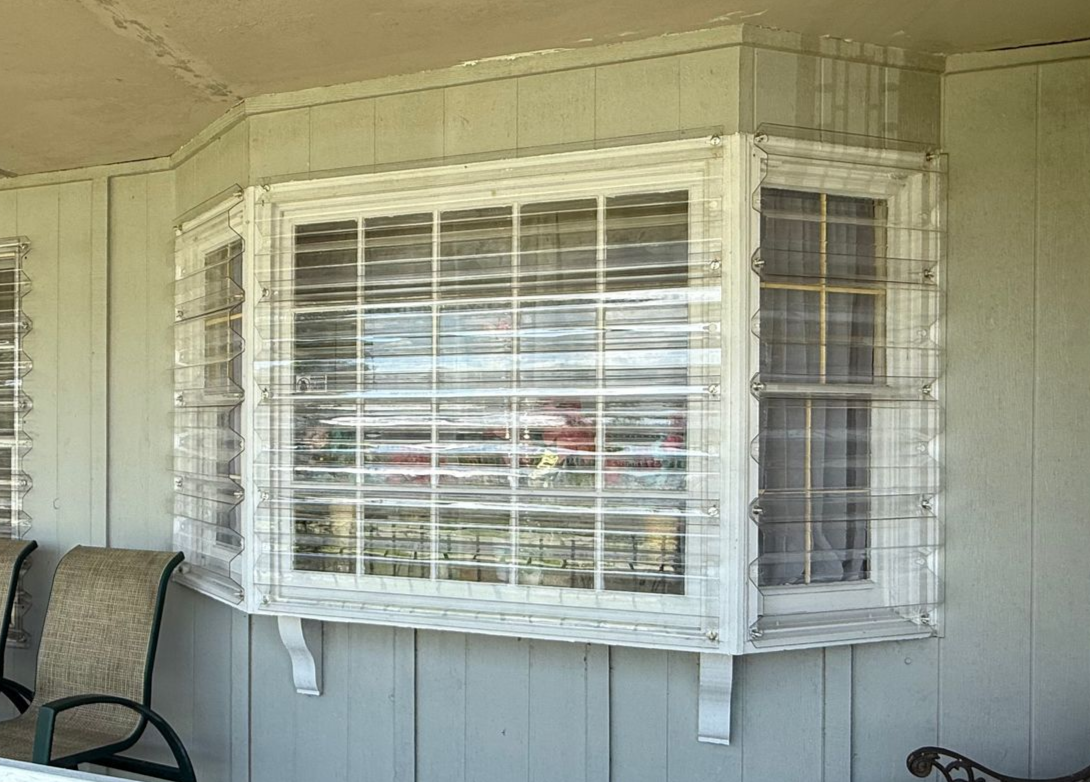 White-framed bay window with closed blinds and grid on a beige exterior wall
