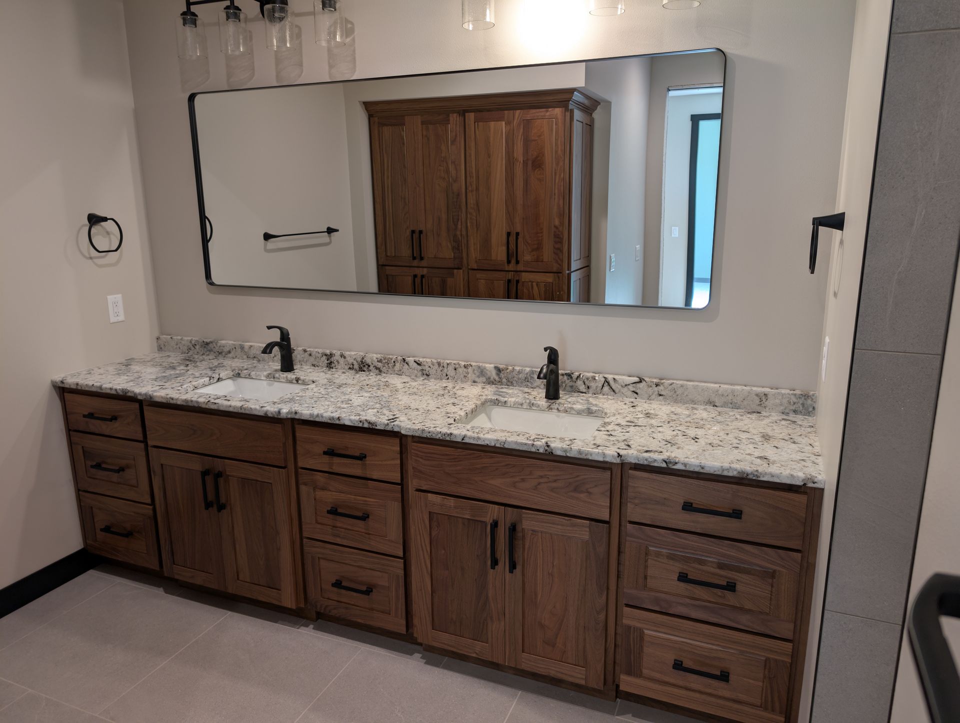 A double vanity bathroom with dark wood cabinets, a speckled stone countertop, two sinks, and a large rectangular mirror. 