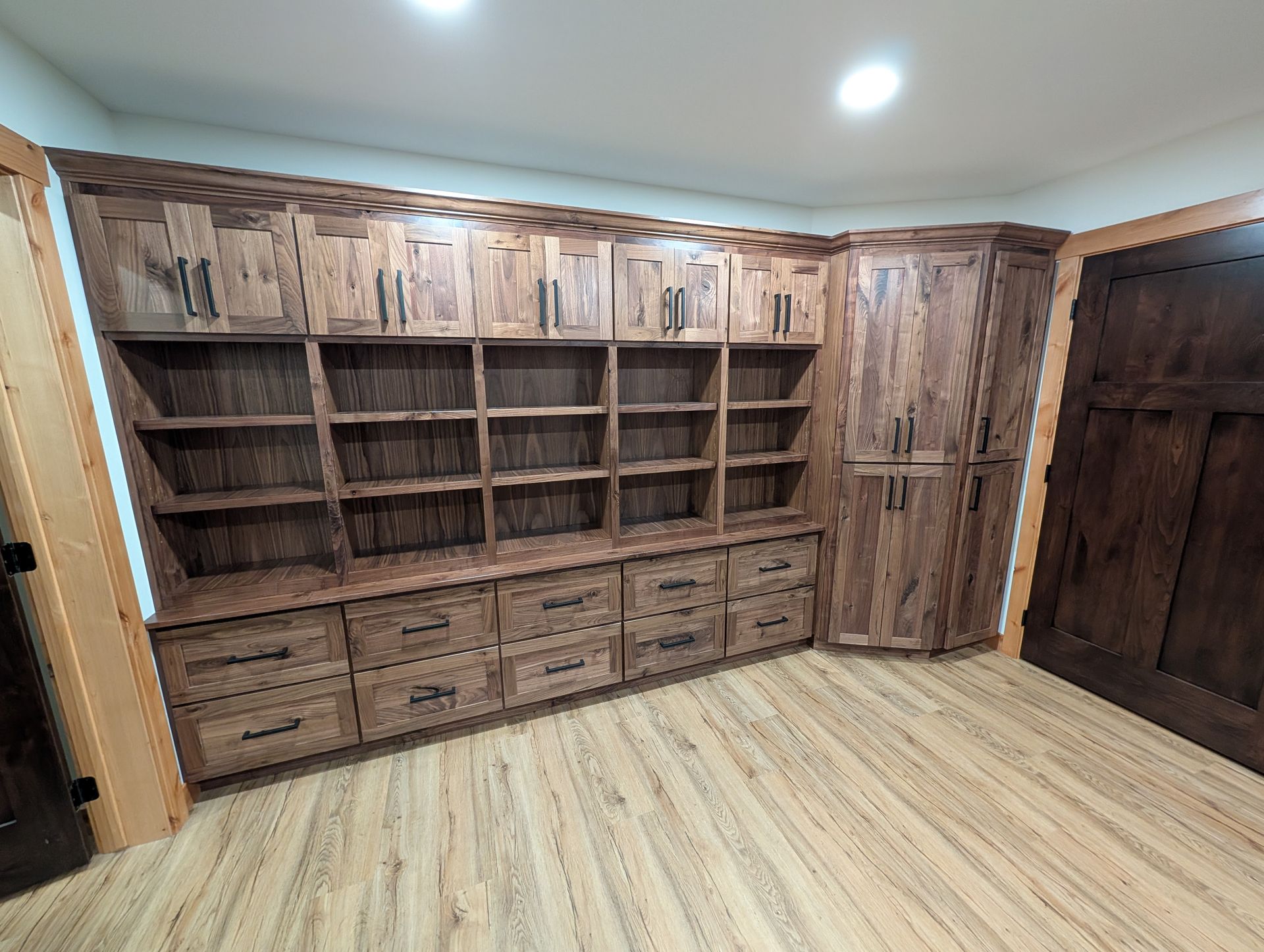 Built-in wall unit with wooden shelving, upper cabinets, and lower drawers in a room with light wood-style flooring. 
