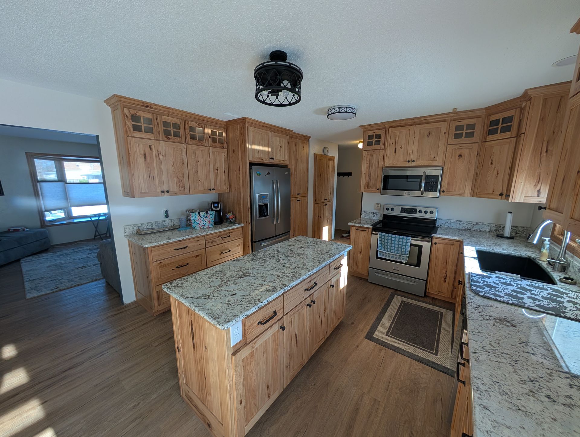 A kitchen with wood cabinetry, a granite-topped island, stainless steel appliances, and a view into a living room. 