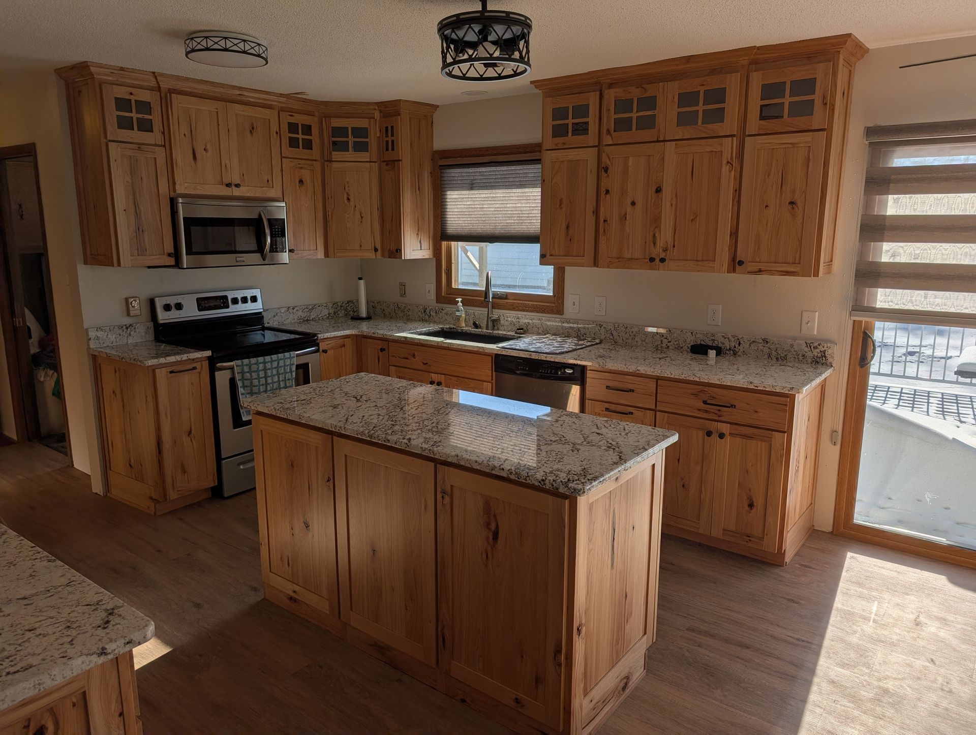 A kitchen featuring rustic wood cabinets, speckled granite countertops, a center island, and stainless steel appliances.