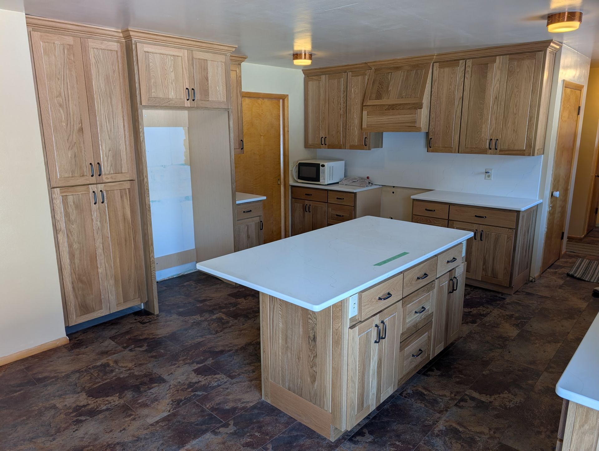 A kitchen featuring light-wood cabinets, a matching island with a white countertop, and dark patterned flooring.