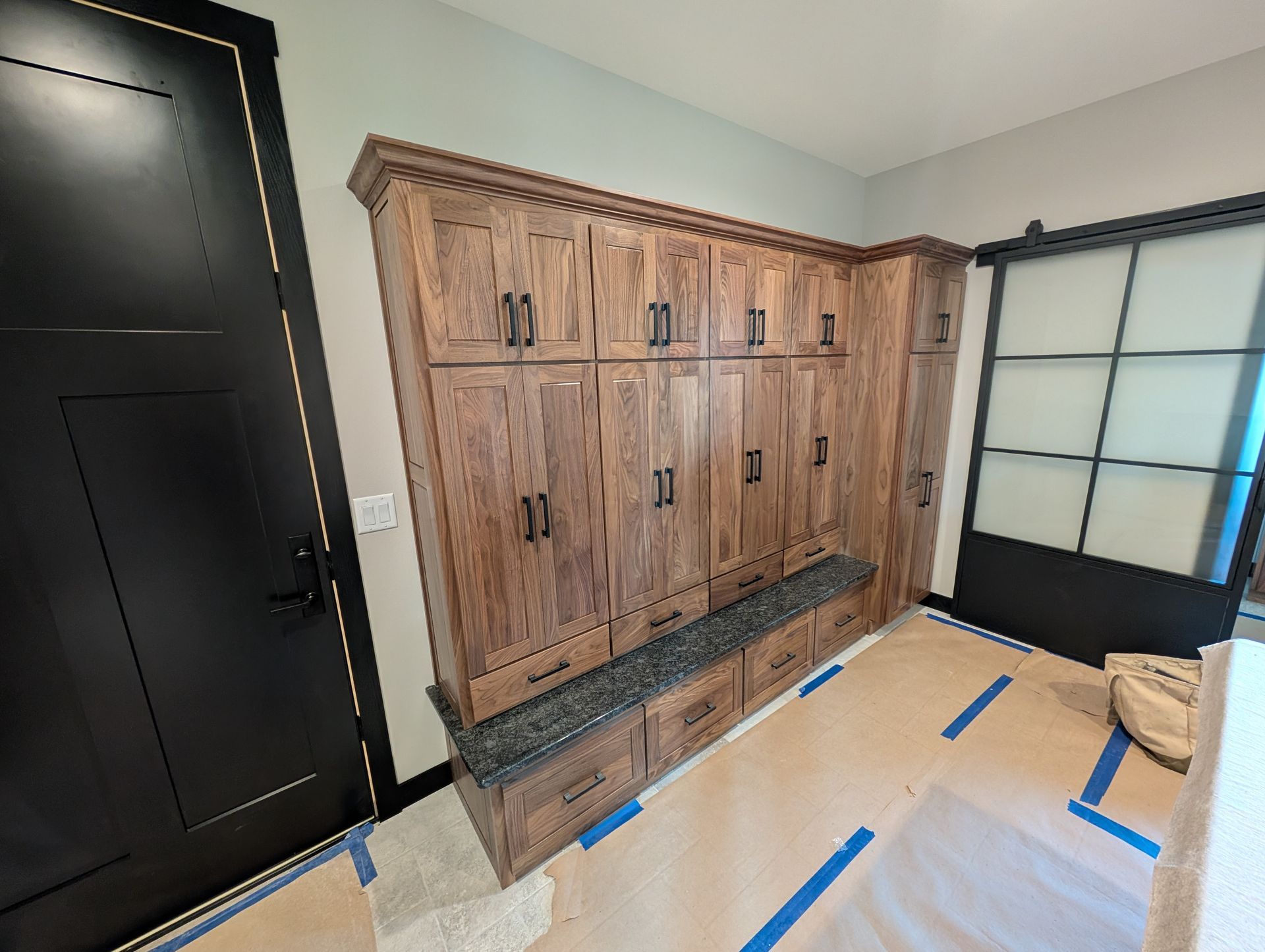 A mudroom with wooden cabinetry, a granite bench, and black accents, featuring a dark door and glass sliding door nearby.