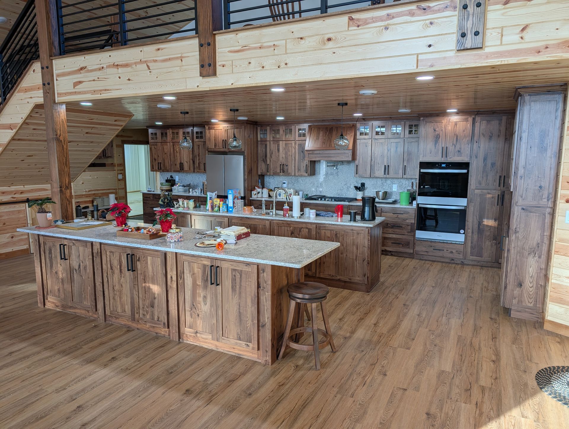 A rustic kitchen with wood cabinets, stone countertops, a large island with a stool, and stainless steel appliances.