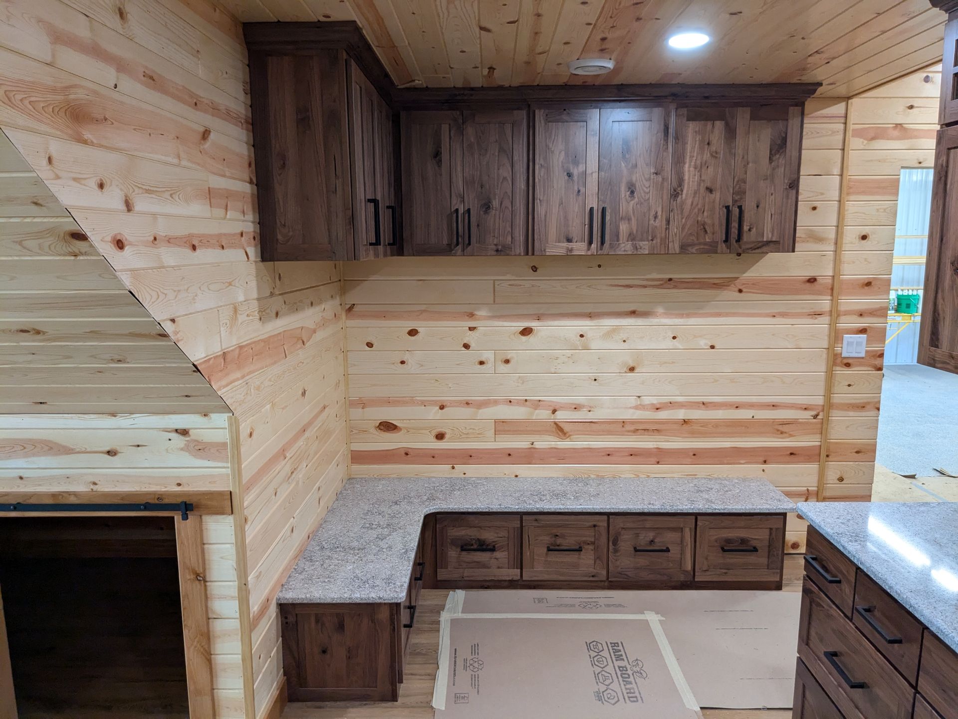 A kitchen area featuring dark wood cabinets, light granite countertops, and knotty pine wood walls and ceiling.