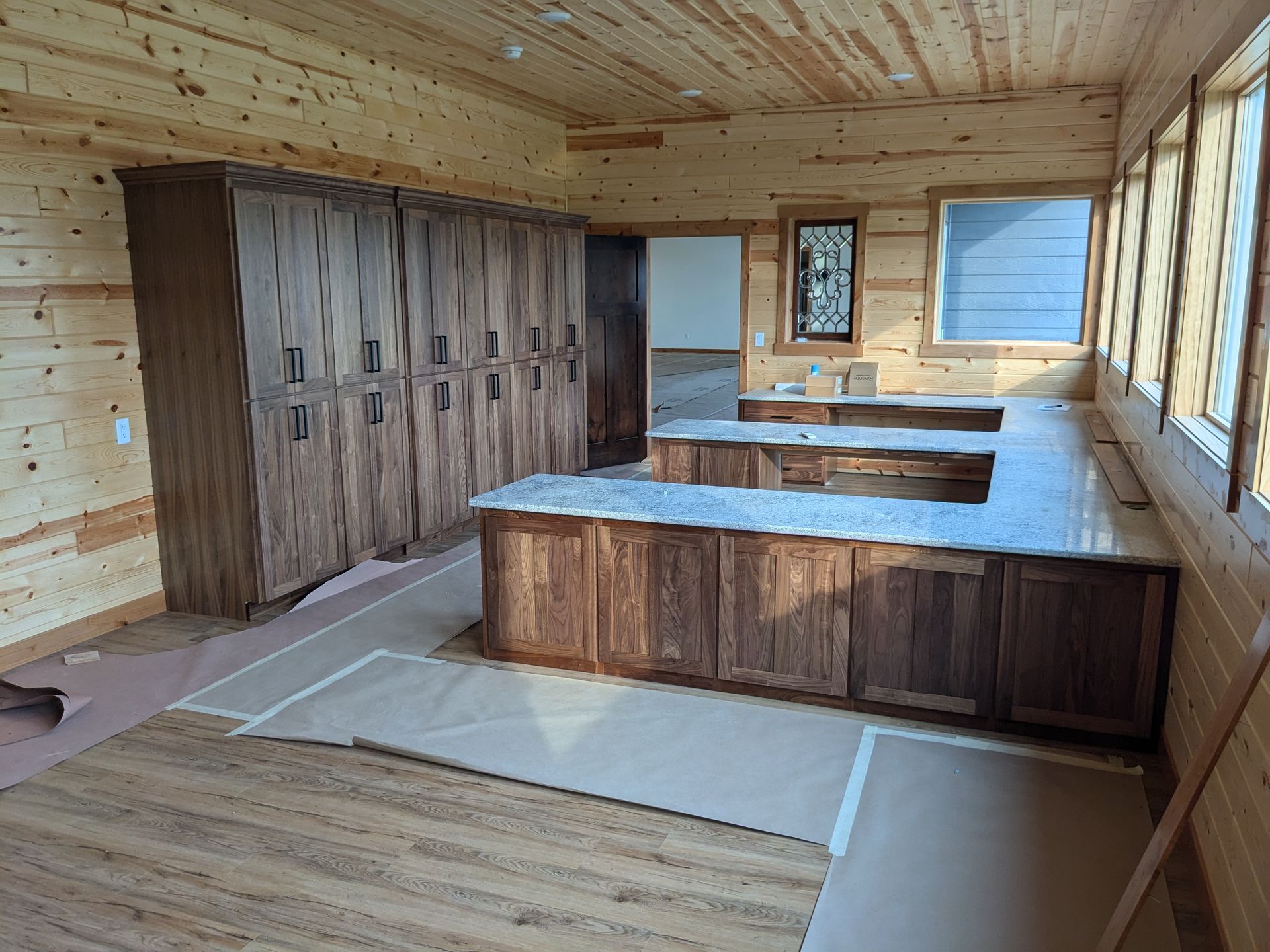 A rustic-style room under construction featuring dark wood cabinets, a U-shaped marble countertop, and pine wood walls.
