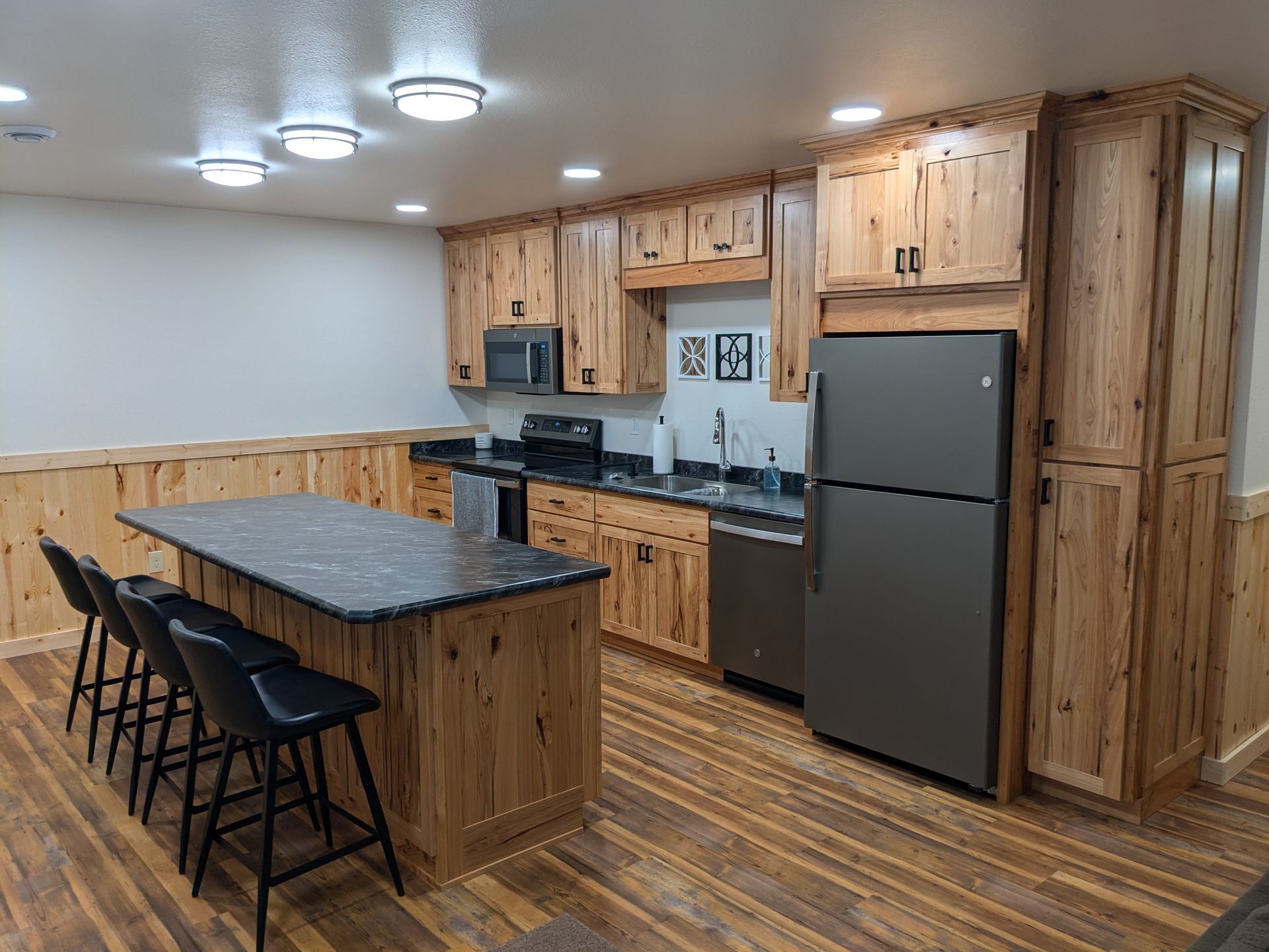 Rustic kitchen featuring hickory wood cabinets, a dark stone island with three stools, and stainless steel appliances.