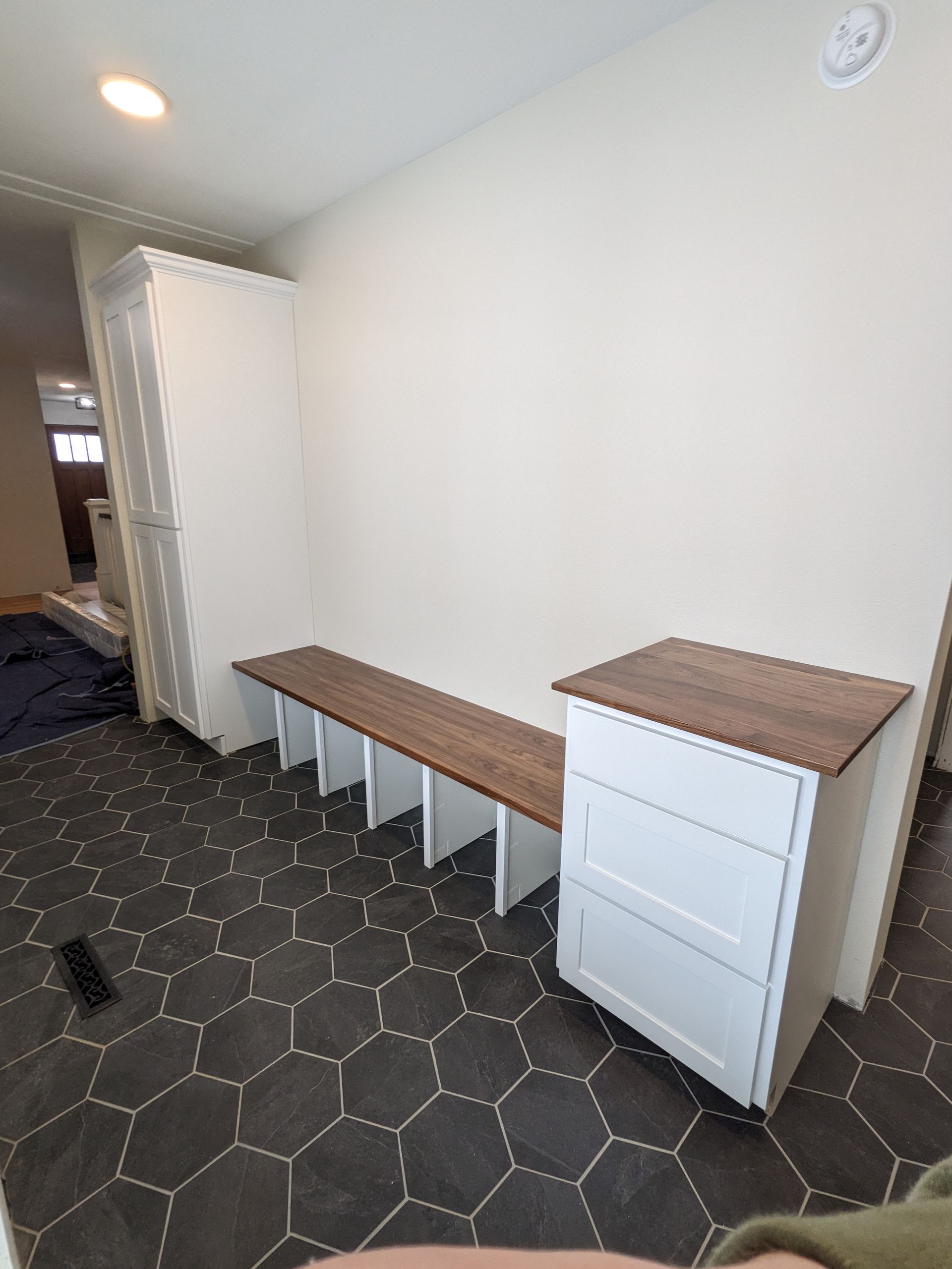 A custom mudroom unit with a tall white cabinet, a long bench with cubbies, and a small white three-drawer dresser unit.