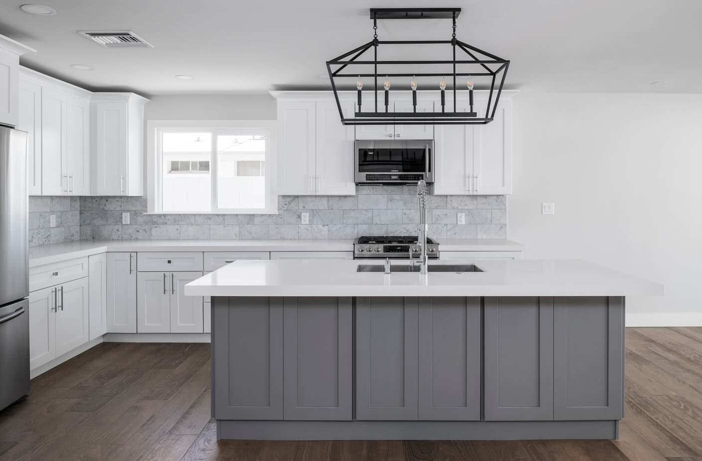 Modern white and gray kitchen with island, stainless steel appliances, and dark wood floors.