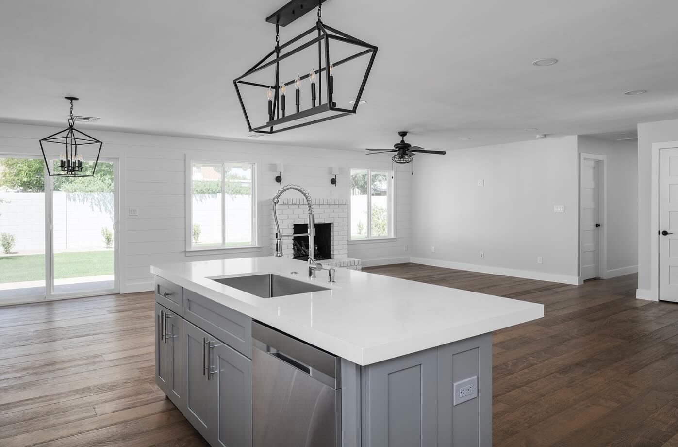 Open-concept kitchen with gray island, white countertops, hardwood floors, and large windows.