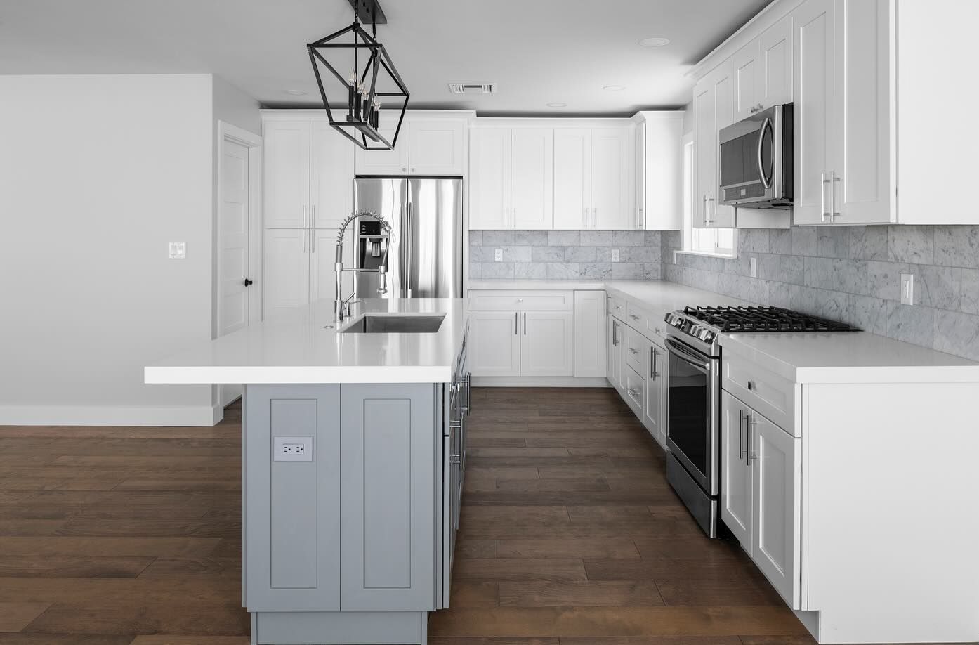 Modern kitchen with white cabinets, gray island, stainless steel appliances, and hardwood floors.
