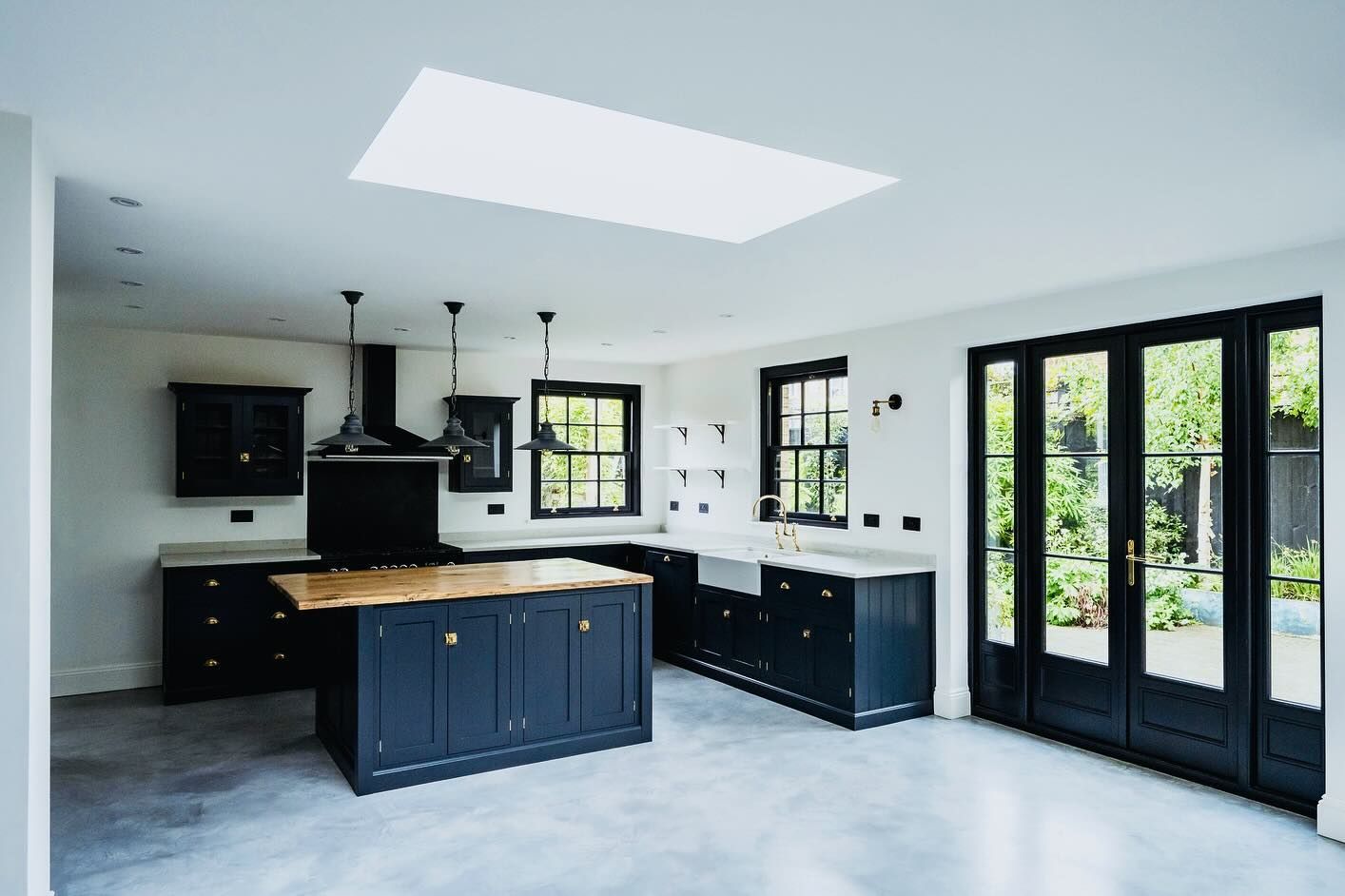 Modern kitchen with dark blue cabinets, wood island, and skylight. French doors lead to a garden.