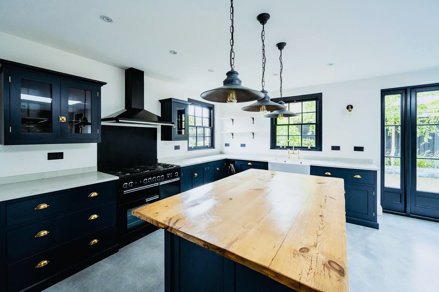 Dark blue kitchen with wooden island, pendant lights, and white countertops.