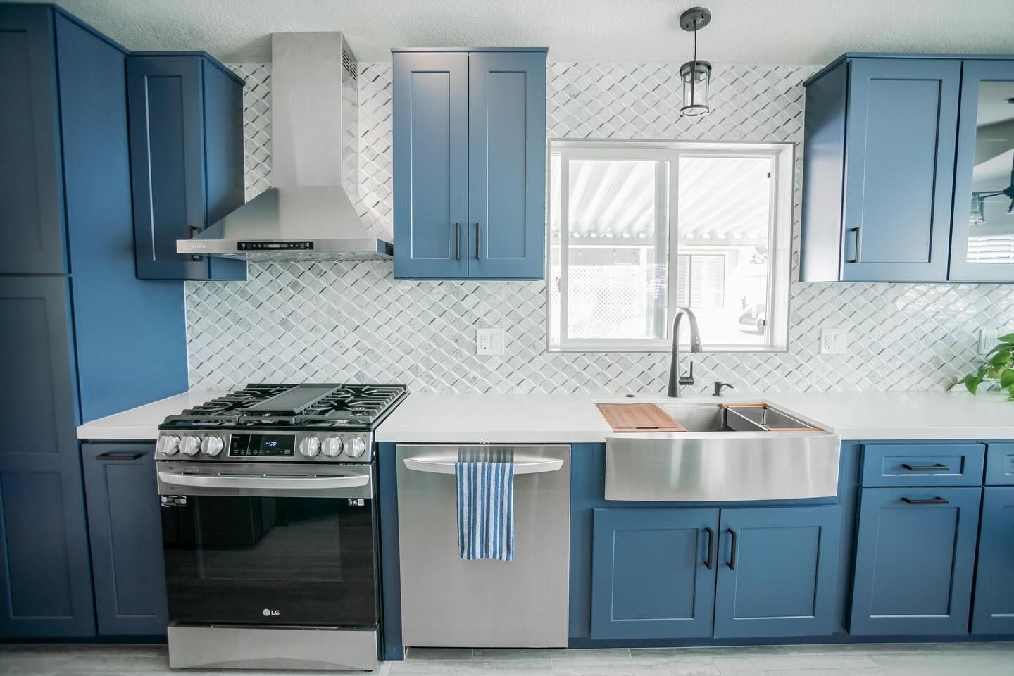 Blue kitchen with stainless steel appliances, white backsplash, and a window.