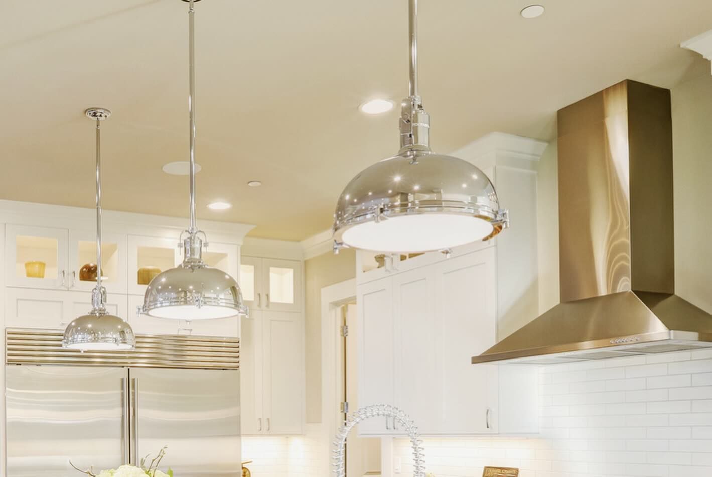 Three chrome pendant lights over a kitchen island, stainless steel range hood.