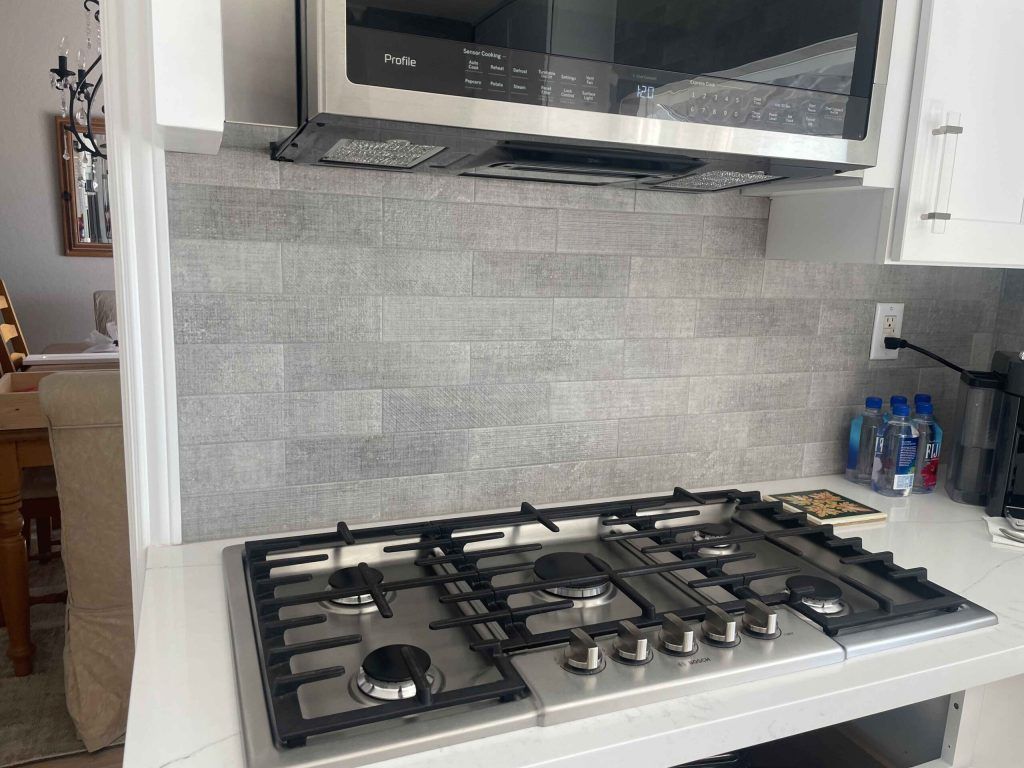 Gas cooktop beneath a microwave. Gray tile backsplash.