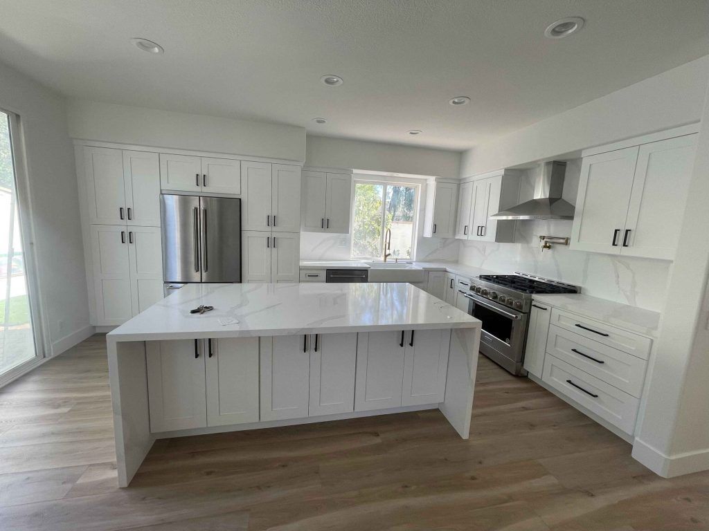 Modern white kitchen with island, stainless steel appliances, and light wood floors.