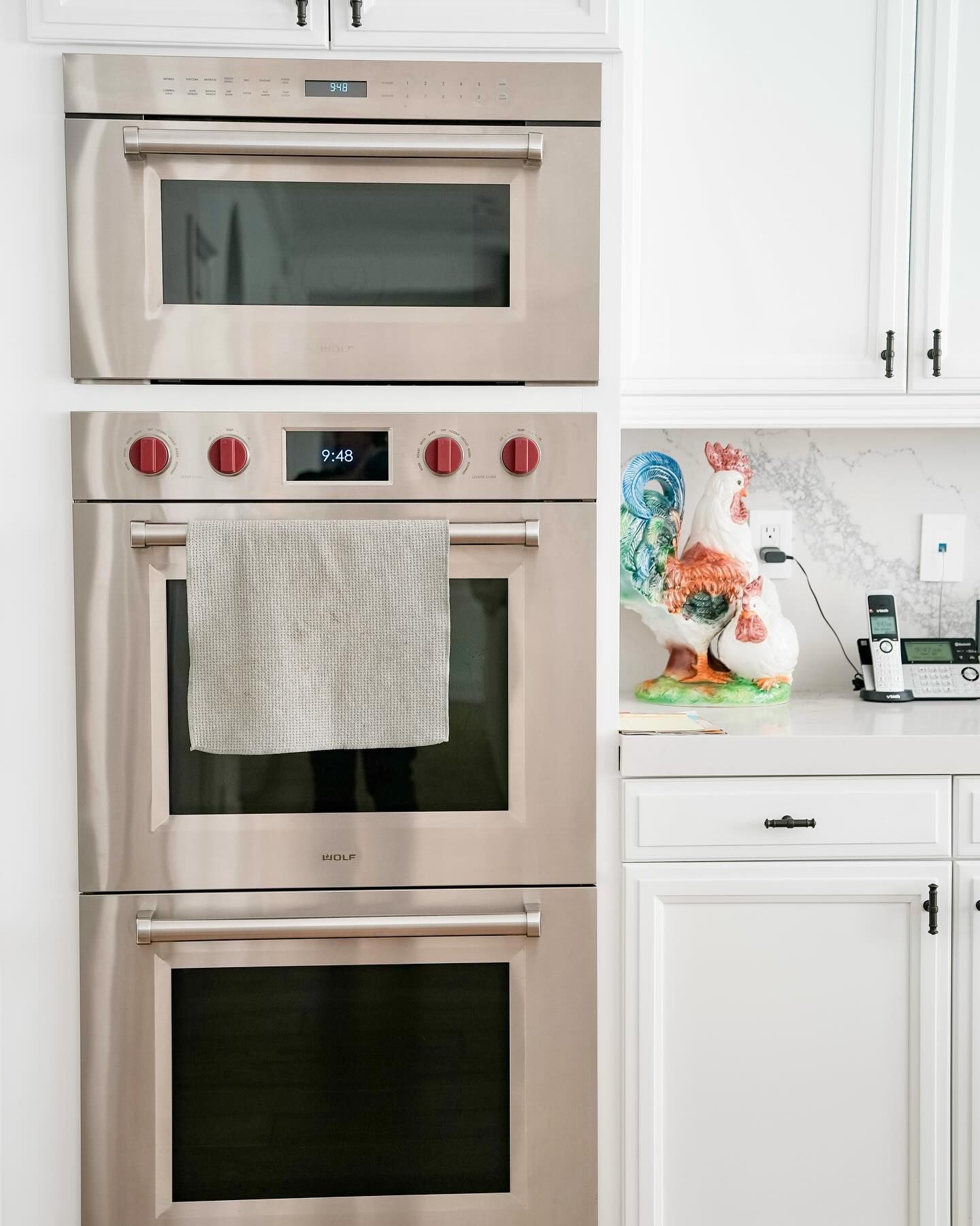 Stainless steel built-in oven and microwave in white kitchen. A decorative rooster sits on the counter.