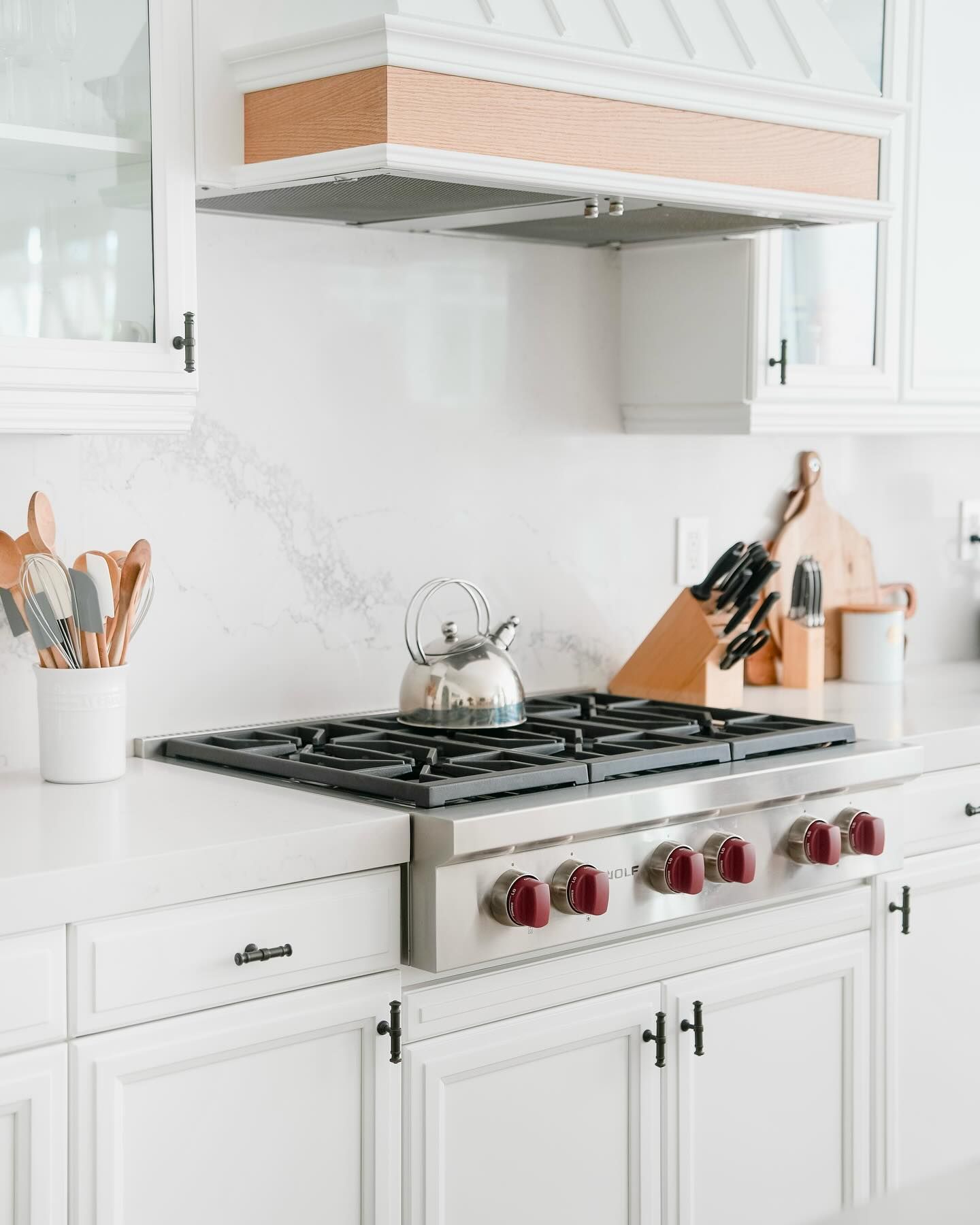 White kitchen with a stainless steel range and wooden accents.