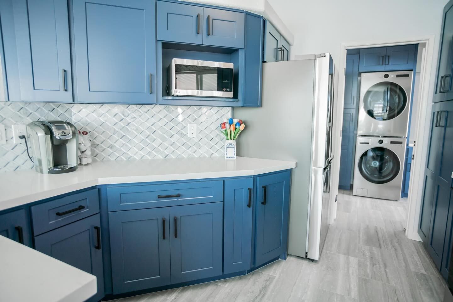 Blue kitchen with white counters, silver appliances, and stacked washer/dryer.