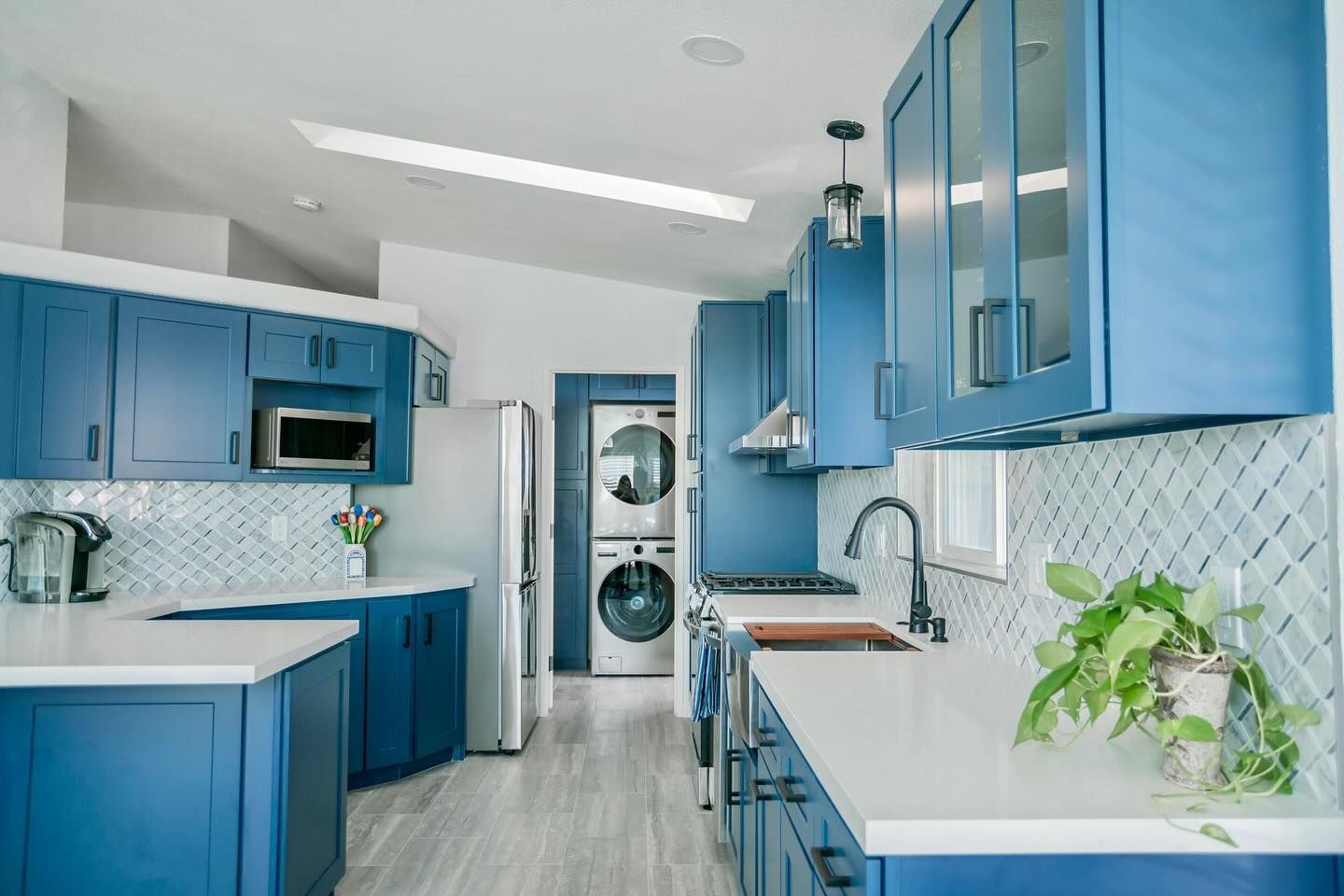 Blue kitchen with white countertops, cabinets, and appliances; grey floors and white backsplash.