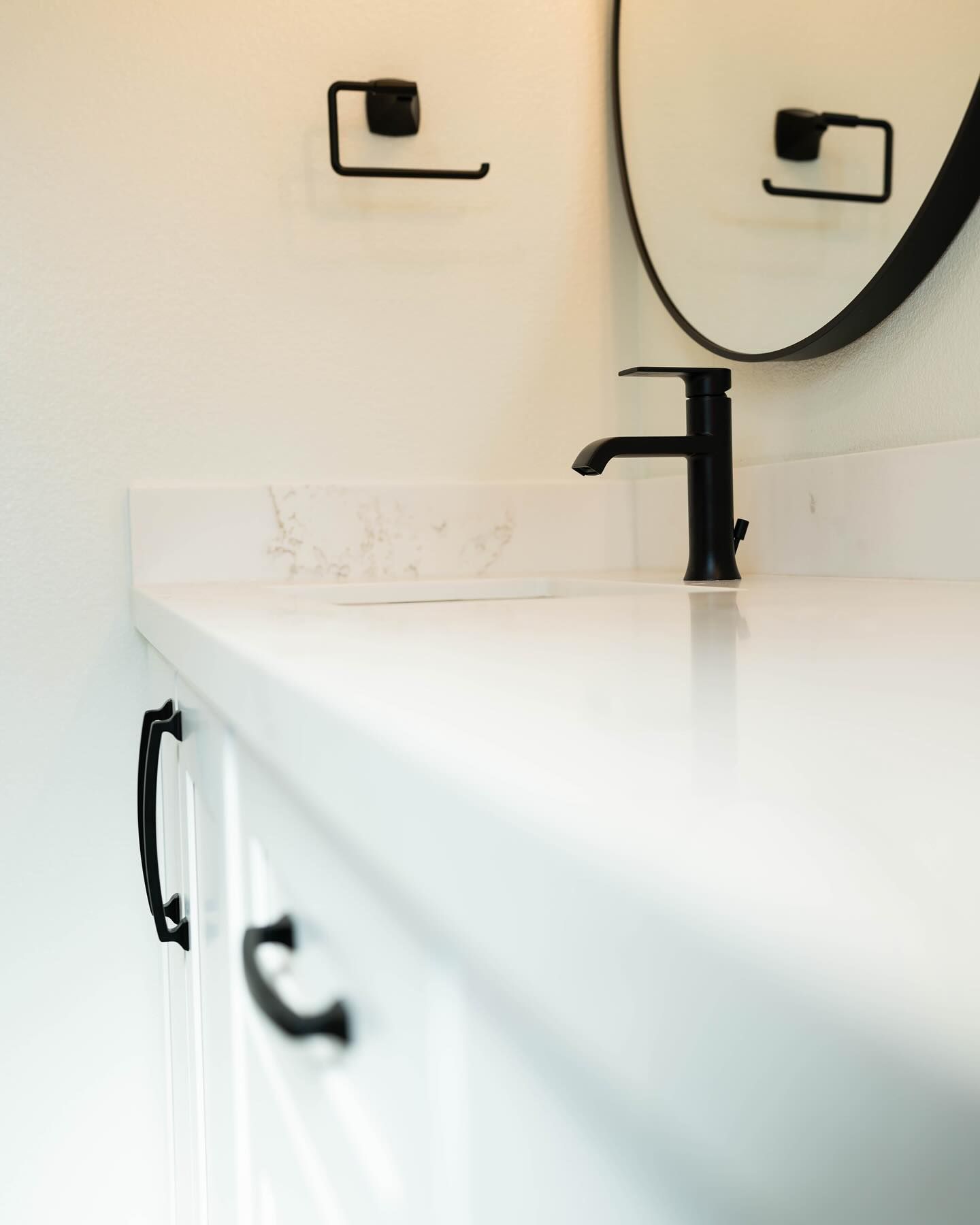 White bathroom countertop with black faucet, drawer pulls, and mirror frame.
