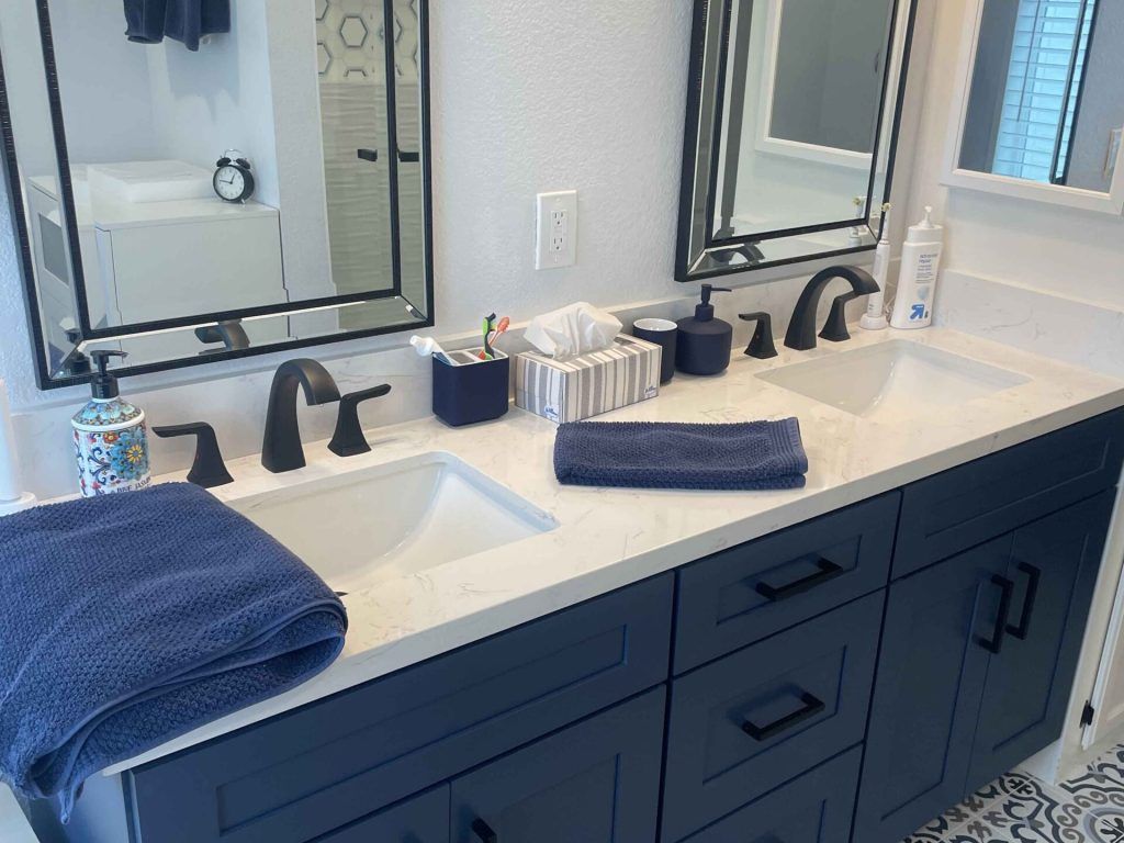 Double sink bathroom vanity with navy cabinets, white countertop, black fixtures and mirrors.