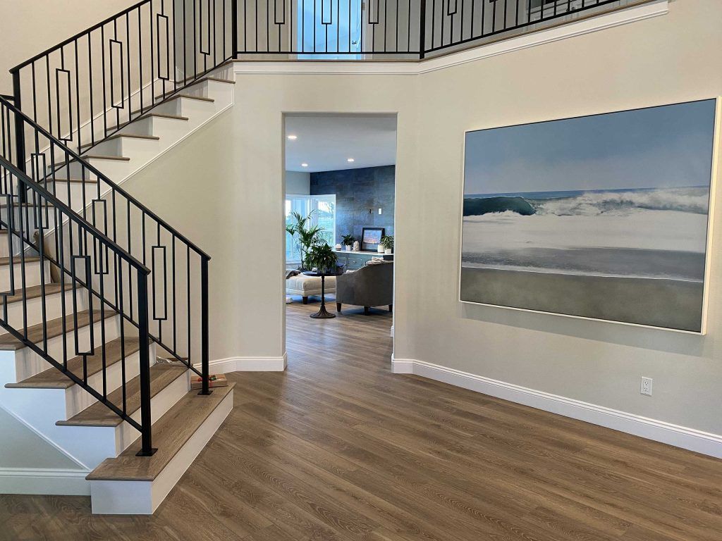 A two-story entryway with stairs and a large ocean painting. Light wood floors and neutral walls.