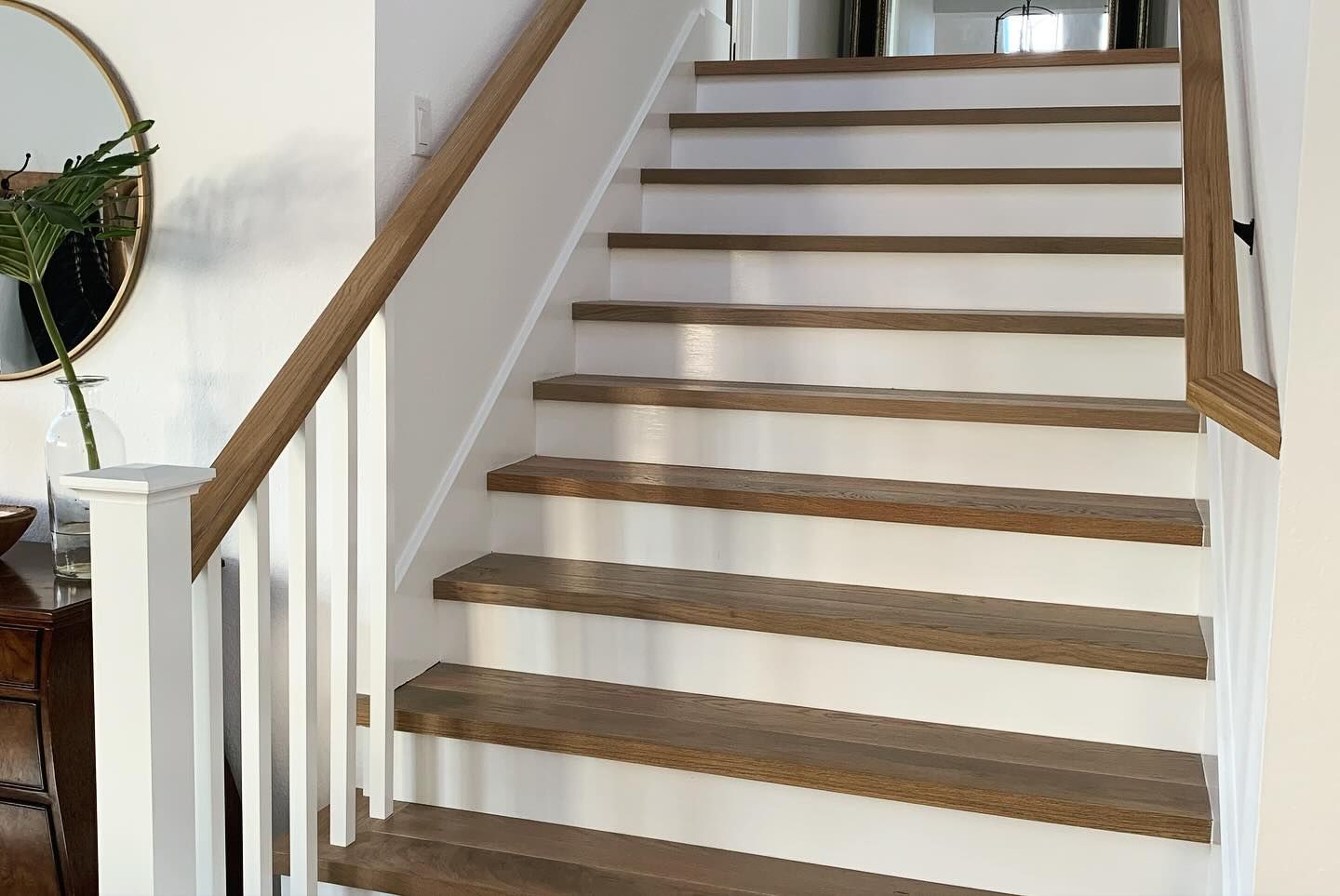 Staircase with wooden steps and railing, white risers, and wall.