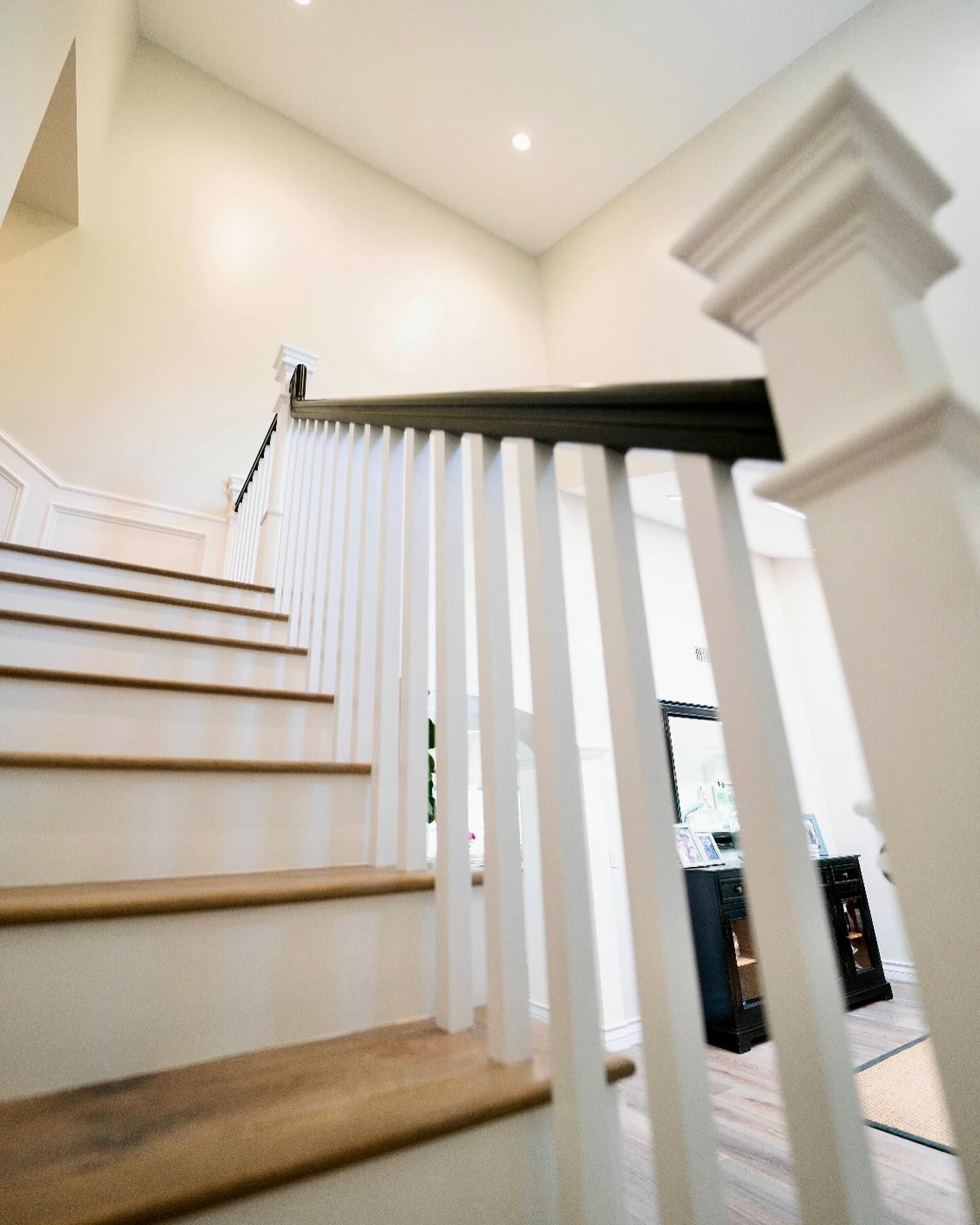 Staircase with white balusters, brown steps, and a dark handrail. Light-colored walls in the background.
