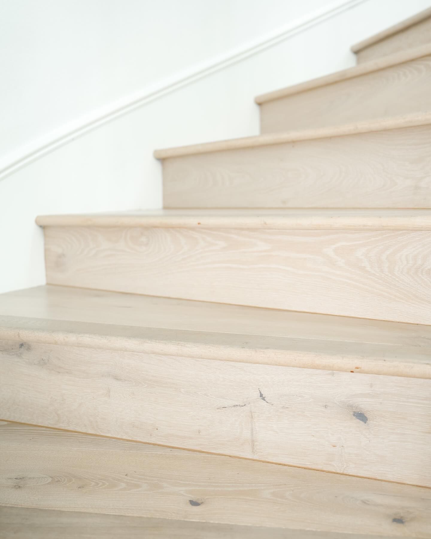 Wooden staircase with light-colored steps and a white wall.
